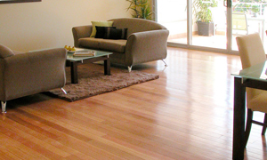 Laminated flooring in a living room with 2 light brown sofas, a rug and a table and chairs