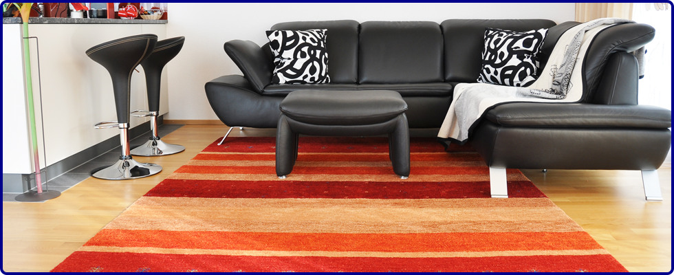 Black leather sofa, foot stool and breakfast bar chairs on wooden flooring on a red, orange and cream rug